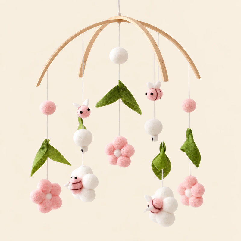Pink Floral Bee hanging mobile with its source-matched wooden support, cords and individual charms on warm beige.