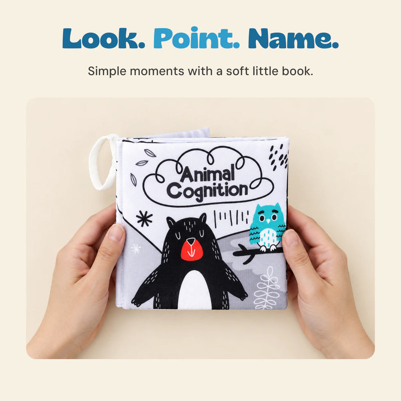 Two adult hands hold the Animal Cognition soft cloth book, keeping the illustrated bear and owl cover visible.
