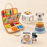 Animal Orange busy board with an off-white and yellow activity cube, ANIMAL lion cloth book and six-ring koala stacking tower on a calm beige background.