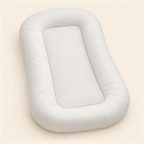 Empty cream SnuggleNest lounger with a rounded padded perimeter and inset centre, shown alone on warm beige.