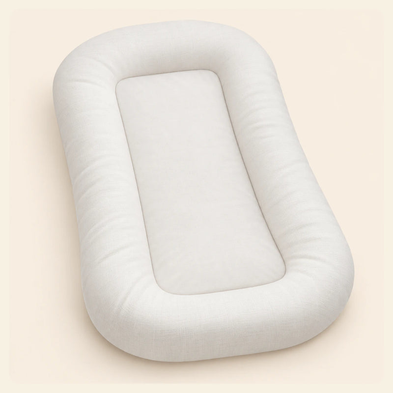 Empty cream SnuggleNest lounger with a rounded padded perimeter and inset centre, shown alone on warm beige.