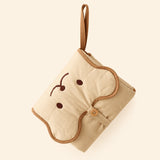 Folded beige changing mat with an embroidered bear face, brown trim, carry loop and wooden button on warm beige.
