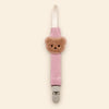 Pink fabric pacifier clip with brown teddy applique, cream loop and grey clasp on a pale warm beige background.