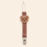 Dusty rose fabric pacifier clip with brown teddy applique, cream loop and grey clasp on a pale warm beige background.