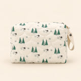 Cream quilted zip pouch with tree print, top zipper and snap wrist loop, on warm beige.