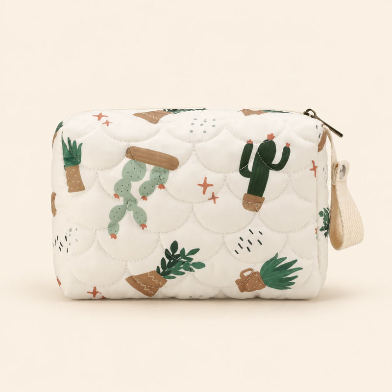 Cream quilted zip pouch with cactus print, top zipper and snap wrist loop, on warm beige.