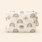 Cream quilted zip pouch with rainbow print, top zipper and snap wrist loop, on warm beige.