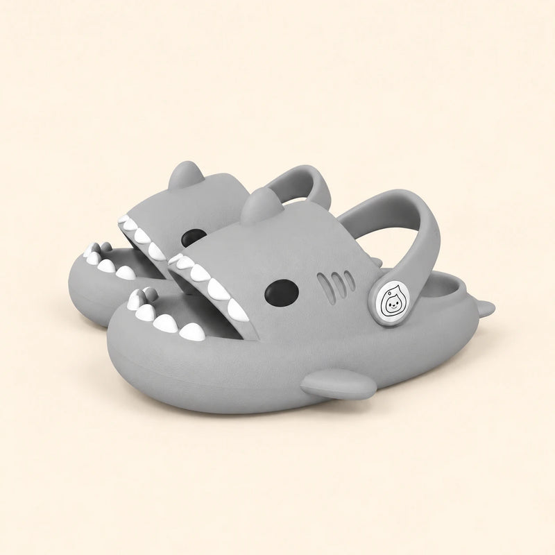 A matching pair of shark slides in the Grey colour on a warm beige background.