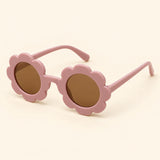 One pair of flower-shaped sunglasses with round brown lenses in the Baby pink colour on a warm beige background.