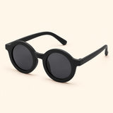 One pair of round sunglasses in the Classic Black option on a warm beige background.