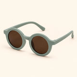 One pair of round sunglasses in the Sage Green option on a warm beige background.