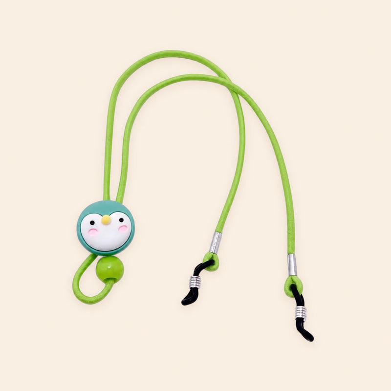 Green cord with penguin charm, sliding bead and two adjustable black end loops on a warm beige background.