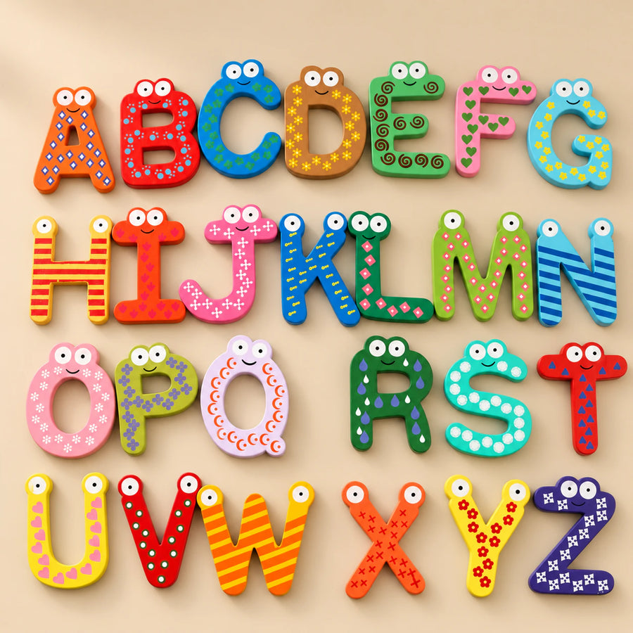 Colourful wooden alphabet letters with painted patterns and smiling faces arranged on a warm beige studio surface.