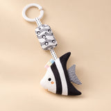 Black and white angelfish hanging rattle with its clip and patterned cushion on a sunlit beige tabletop.