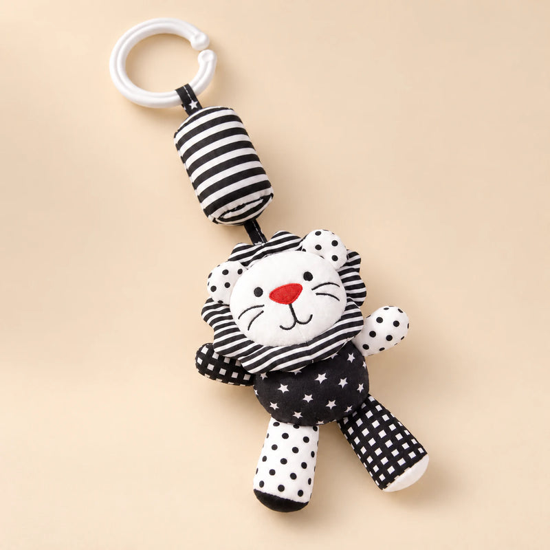 Black and white lion hanging rattle with its clip and patterned cushion on a sunlit beige tabletop.