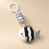 Black and white round fish hanging rattle with its clip and patterned cushion on a sunlit beige tabletop.