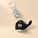 Black and white whale hanging rattle with its clip and patterned cushion on a sunlit beige tabletop.
