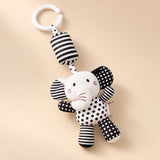 Black and white elephant hanging rattle with its clip and patterned cushion on a sunlit beige tabletop.