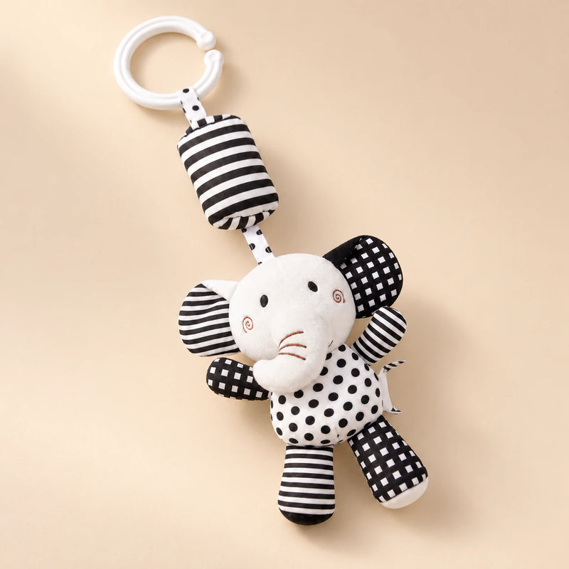 Black and white elephant hanging rattle with its clip and patterned cushion on a sunlit beige tabletop.