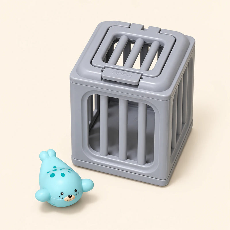 One pale turquoise spotted seal toy beside one gray rescue cage on a warm beige background. This is one separate variant choice.