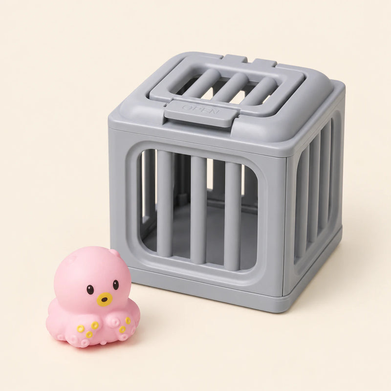 One pink octopus with yellow details toy beside one gray rescue cage on a warm beige background. This is one separate variant choice.