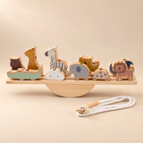 A wooden animal balance set on a straight plank and semicircular rocker, with a cotton threading cord in warm daylight.