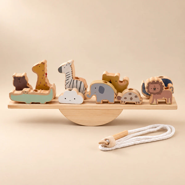 A wooden animal balance set on a straight plank and semicircular rocker, with a cotton threading cord in warm daylight.