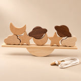 Two moons, two stars, two clouds and two planet-shaped pieces on a straight wooden balance plank, with a semicircular rocker and threading cord.