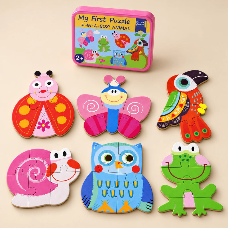 A storage tin and six assembled puzzles showing ladybird, butterfly, toucan, snail, owl and frog on a sunlit beige table.