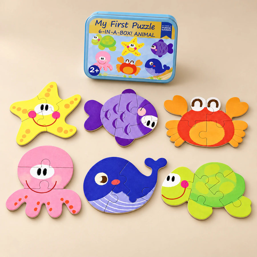 A storage tin and six assembled puzzles showing starfish, fish, crab, octopus, whale and turtle on a sunlit beige table.