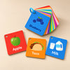 Food Friends flashcards with Apple, Taco and Milk cards beside a ring-bound Blueberry stack in warm natural light.
