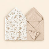 Two hooded towels, one white with brown floral print and one plain oat beige. Shown on warm beige.