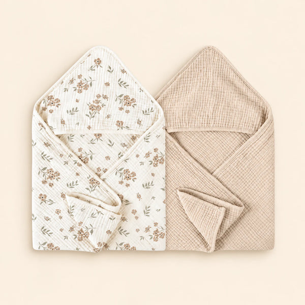 Two hooded towels, one white with brown floral print and one plain oat beige. Shown on warm beige.