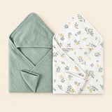 Two hooded towels, one plain sage green and one white with a yellow floral and green leaf print. Shown on warm beige.