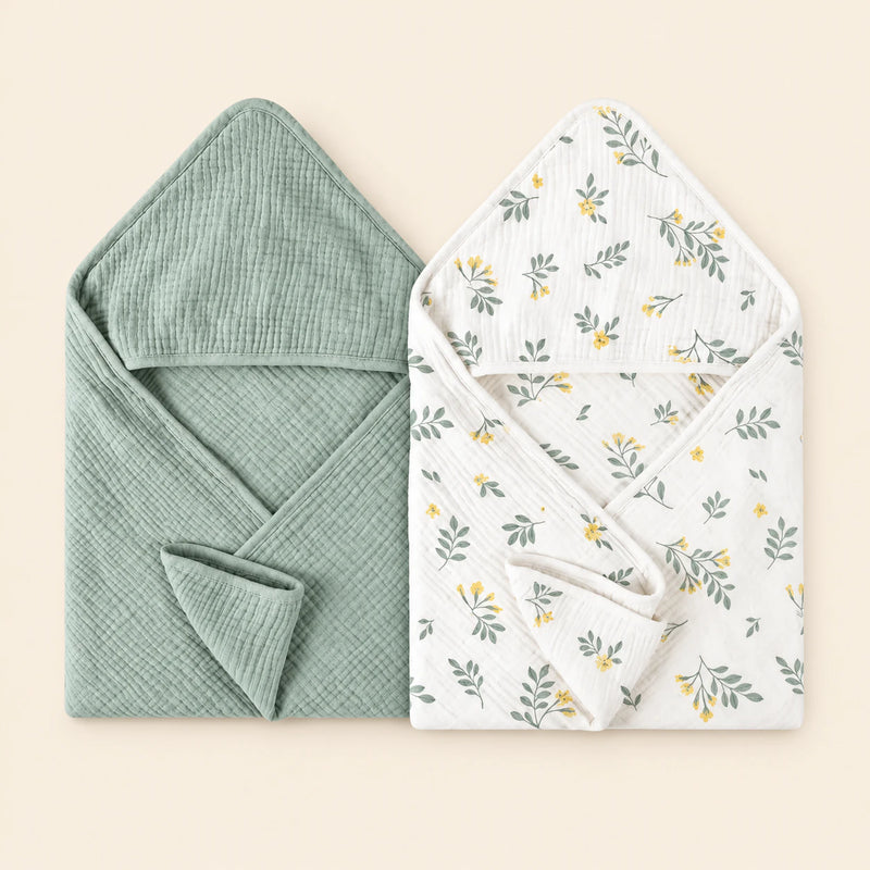 Two hooded towels, one plain sage green and one white with a yellow floral and green leaf print. Shown on warm beige.
