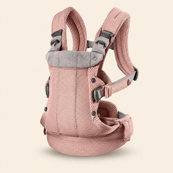 Pink baby carrier with mesh panels, padded shoulder straps, buckles and a broad waist band, shown alone on warm beige.