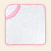 White hooded towel with pink edge binding, laid flat alone on warm beige.