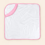 White hooded towel with pink edge binding, laid flat alone on warm beige.