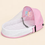 Open blush pink tent with a white mesh canopy, padded oval interior and three hanging animal toys on warm beige.