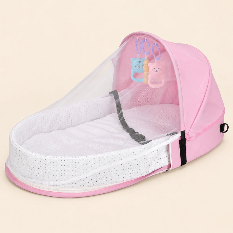 Open blush pink tent with a white mesh canopy, padded oval interior and three hanging animal toys on warm beige.