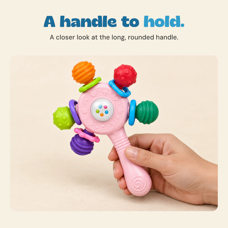 An adult hand holds the pink rattle handle while all five textured ends remain visible.