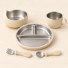 Oat Dine Set with empty three-section stainless steel plate, bowl, single-handled cup, spoon and fork on warm beige.