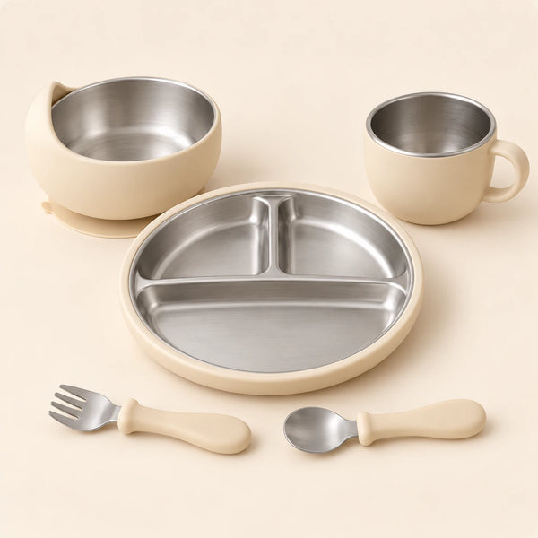 Oat Dine Set with empty three-section stainless steel plate, bowl, single-handled cup, spoon and fork on warm beige.