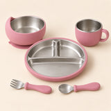 Rose Dine Set with empty three-section stainless steel plate, bowl, single-handled cup, spoon and fork on warm beige.