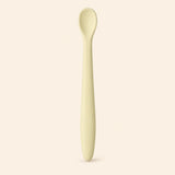 Oat silicone baby feeding spoon, showing its slim handle and shallow oval bowl on warm beige.