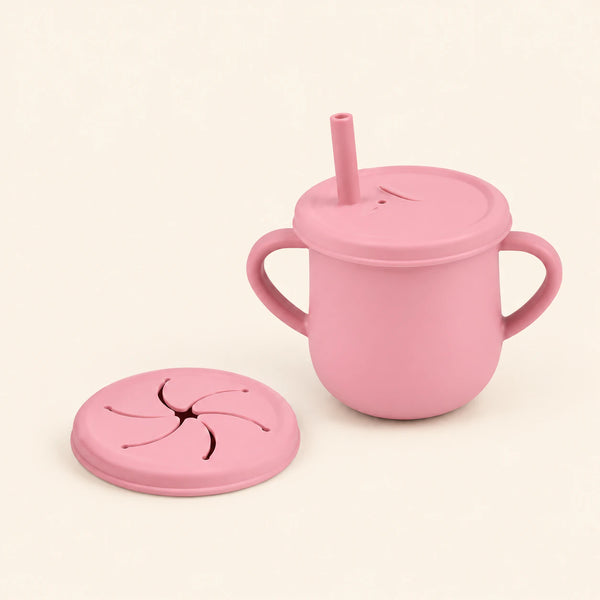 Blush Pink silicone cup with two side handles, fitted straw lid and straw, plus a separate snack lid on warm beige.
