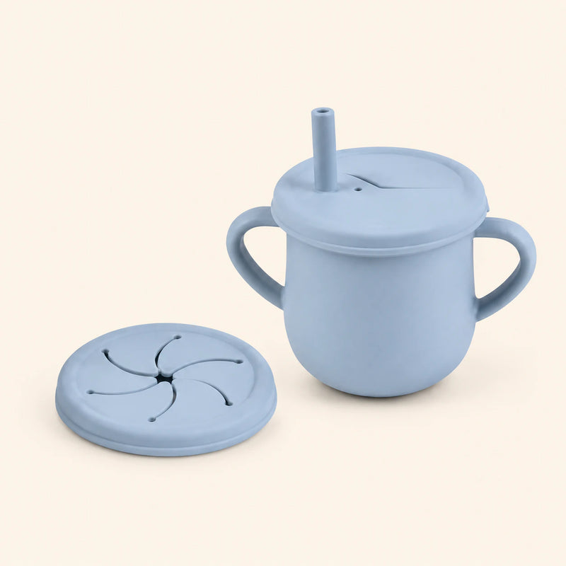 Sky Blue silicone cup with two side handles, fitted straw lid and straw, plus a separate snack lid on warm beige.