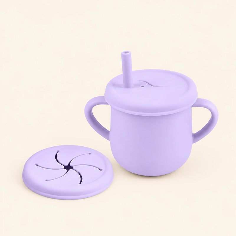 Lilac silicone cup with two side handles, fitted straw lid and straw, plus a separate snack lid on warm beige.