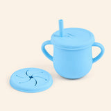 Aqua Blue silicone cup with two side handles, fitted straw lid and straw, plus a separate snack lid on warm beige.