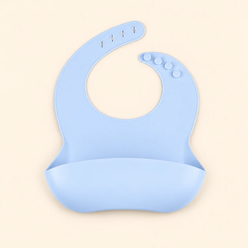 Sky Blue silicone catch bib, with a scoop pocket and adjustable button-and-hole neck closure, on warm beige.